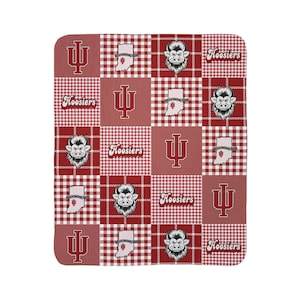 Op de afbeelding: Een rood-wit patchwork deken met het Indiana University logo, het woord "Hoosiers", een cartoon gorilla en de omtrek van de staat Indiana. De deken heeft een hondenpoottand patroon.
