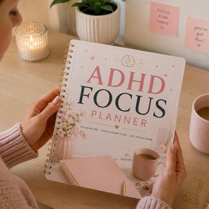 Puede incluir: Una agenda de espiral ADHD Focus Planner con una cubierta blanca que presenta texto en rosa y negro, un icono de cerebro y una ilustración de un jarrón con flores. La cubierta incluye el texto ADHD FOCUS PLANNER y el subtítulo FOCUS BETTER - AVOID DISTRACTIONS - GET THINGS DONE.