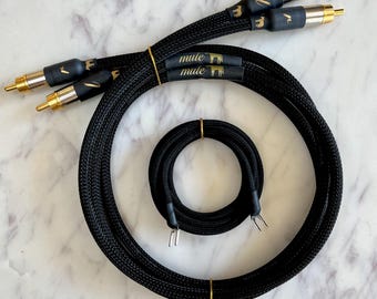 May include: Black audio cables with gold-colored connectors and accents. The cables are arranged in a circular pattern, with the text "mule" printed on the cable. The cables are tied with gold-colored ties.