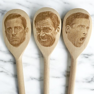 Peut inclure: Trois cuillères en bois avec des visages gravés. Chaque cuillère présente une expression faciale différente. Les cuillères sont en bois de couleur claire et sont disposées sur une surface en marbre blanc. Un ensemble d'ustensiles de cuisine unique.
