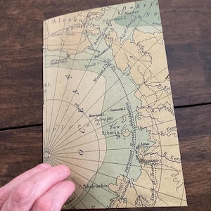 May include: A vintage map of the Arctic region, showing the coastline of Alaska, Siberia, and the Bering Strait. The map is printed on aged paper with a light brown background and green and blue markings. The map includes text labels for various geographic features, including "Alaska", "Siberia", "Bering Strait", and "Arctic Circle".