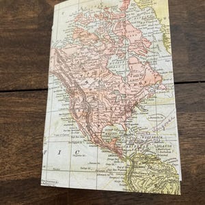 May include: An antique map of North and South America, printed on paper with a yellowed tint. The map shows the continents in shades of pink, green, and yellow, with the oceans in blue. The map includes text labels for various locations, including cities, rivers, and mountains.