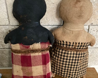 May include: Two handmade rag dolls, one with black fabric and a red and white checkered skirt, the other with brown fabric and a black and white checkered skirt.