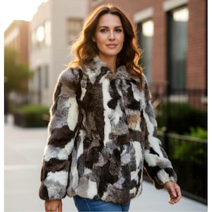 May include: A patterned fur jacket in shades of brown, white, and grey. The jacket features a collared neckline and long sleeves. The woman is wearing blue jeans.