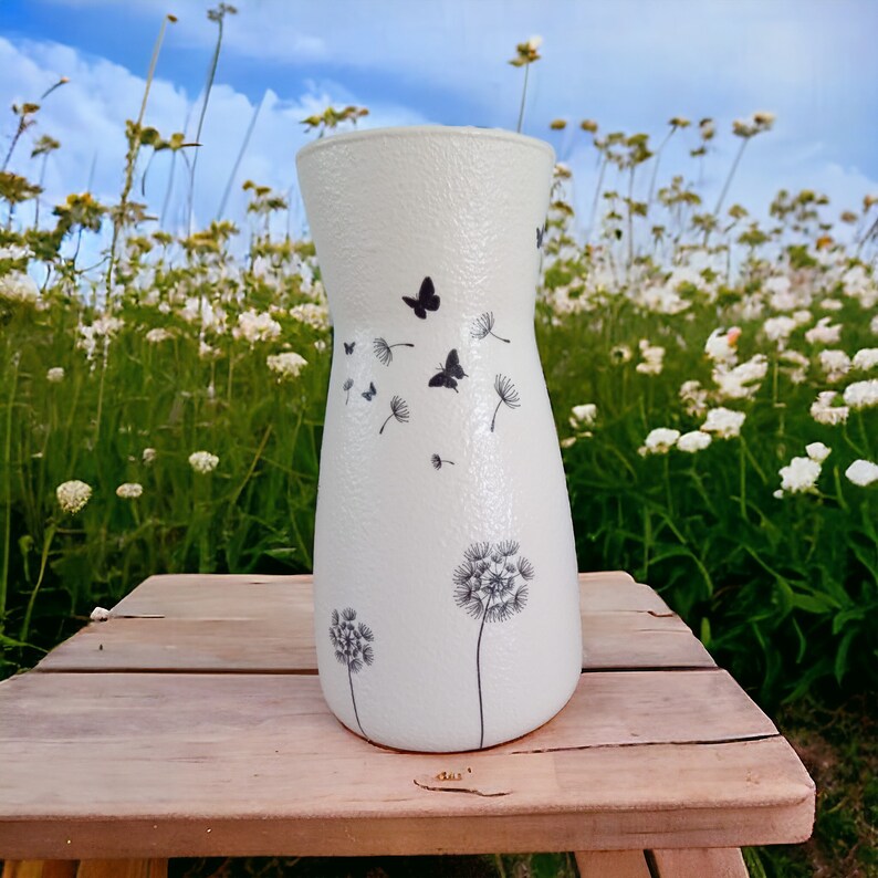 May include: White ceramic vase with a textured surface and a black and white design of butterflies and dandelions.