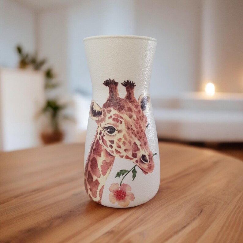 May include: White ceramic vase with a watercolor illustration of a giraffe's head with a pink flower in its mouth.