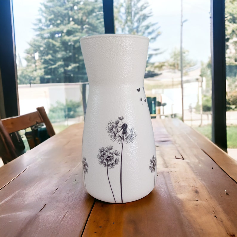 May include: White ceramic vase with a textured surface and a design of black dandelions and butterflies.