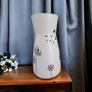 May include: A white ceramic vase with a textured surface and a design of black dandelions and butterflies.