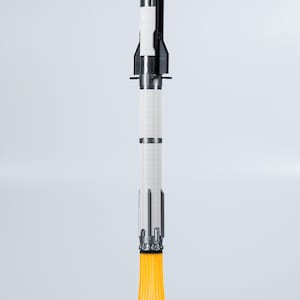 May include: A model rocket with a black and silver nose cone, a white cylindrical body, and silver accents. The rocket sits on a white cloud-shaped base with orange flames emanating from the bottom, suggesting liftoff.