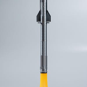 May include: A silver and black rocket model with a yellow flame effect at the base, resting on a white cloud-like structure. The rocket has a detailed design, with fins and a pointed nose. The model is a space-themed item.