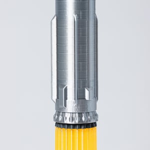 May include: A 3D-printed rocket model with a silver-gray upper section and a bright yellow lower section. The upper section has a textured surface with detailed paneling, while the lower section features vertical ridges. The rocket is set against a plain white background.