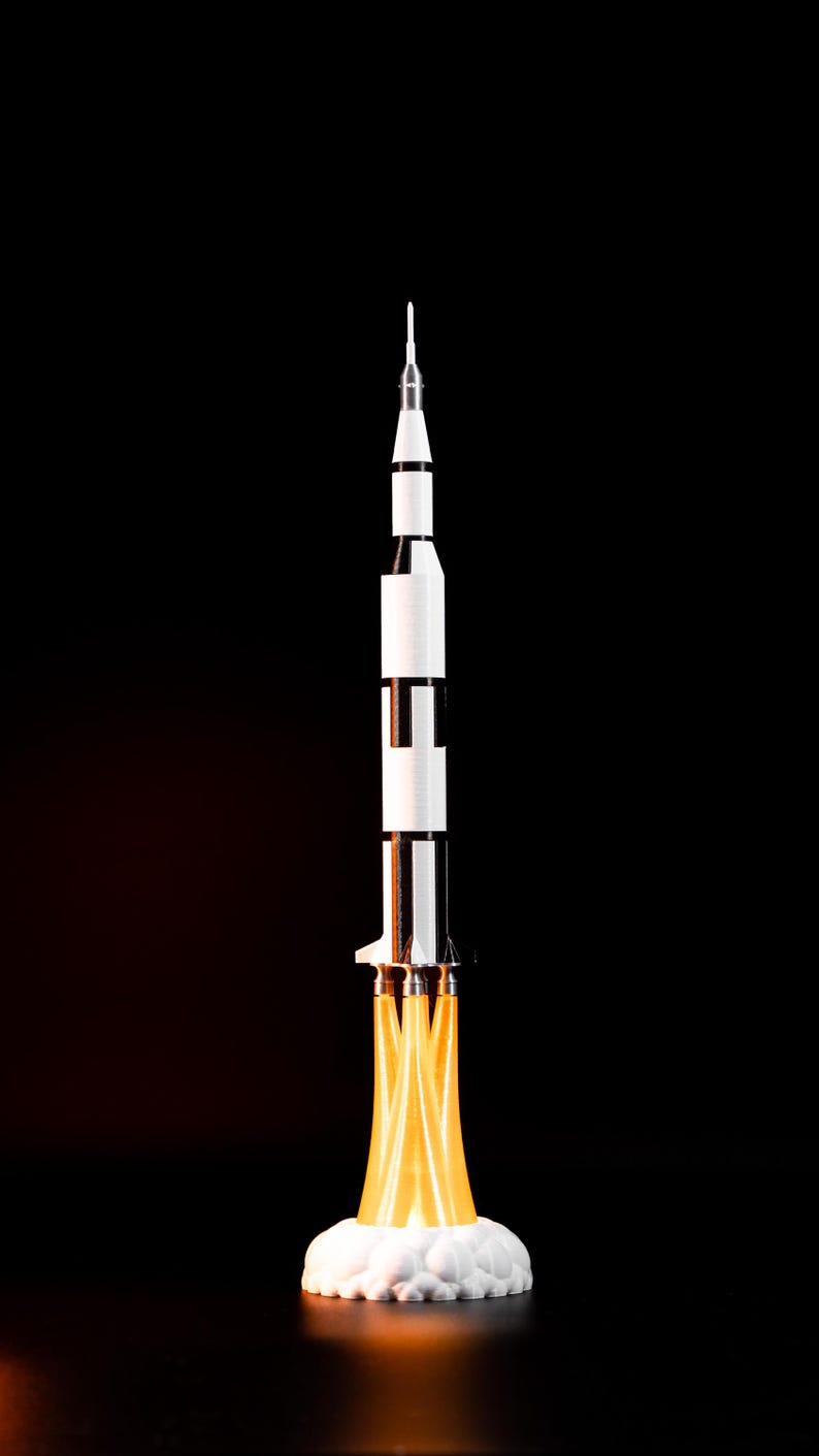 May include: A model rocket ship with a white and black body, a pointed top, and a fiery orange exhaust. The rocket is set against a black background, giving the impression of a launch.