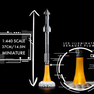 May include: A miniature silver and white rocket model with an LED illuminated exhaust plume. The model is 14.5 inches tall and is labeled as 1:440 scale. The rocket is set against a black background.