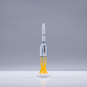 May include: A white and blue toy rocket with yellow flames blasting from the base. The rocket has a pointed top and several gray bands around the body. The rocket is on a white surface against a gray background.
