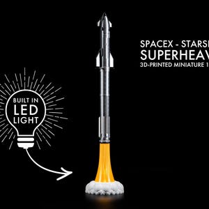 May include: A 3D-printed miniature of the SpaceX Starship Superheavy rocket, scale 1:440. The silver and black rocket has a yellow flame effect at the base, with a white cloud of smoke. The model has a built-in LED light.