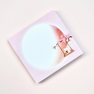 May include: Pink sticky note with a white cat sitting on a swing in a cherry blossom tree. The background is a gradient of pink and white with a large circle in the center.