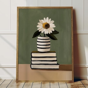 May include: A framed art print depicting a still life scene. A white daisy with a yellow centre and green leaves is in a black and white striped vase on a stack of books with black and white stripes. The background is olive green.