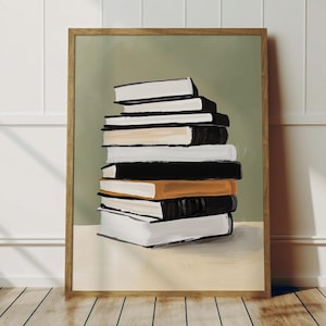 May include: A framed art print featuring a stack of books. The books have white, black, and orange covers. The background is a muted green, and the frame is a light brown. The artwork is displayed on a white surface.