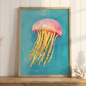 K&ouml;nnte beinhalten: Gerahmtes Gem&auml;lde einer Qualle. Die Qualle ist rosa und gelb mit langen, flie&szlig;enden Tentakeln vor einem t&uuml;rkisfarbenen Hintergrund. Das Kunstwerk wird auf einem Holzschrank mit dekorativen Gegenst&auml;nden ausgestellt.
