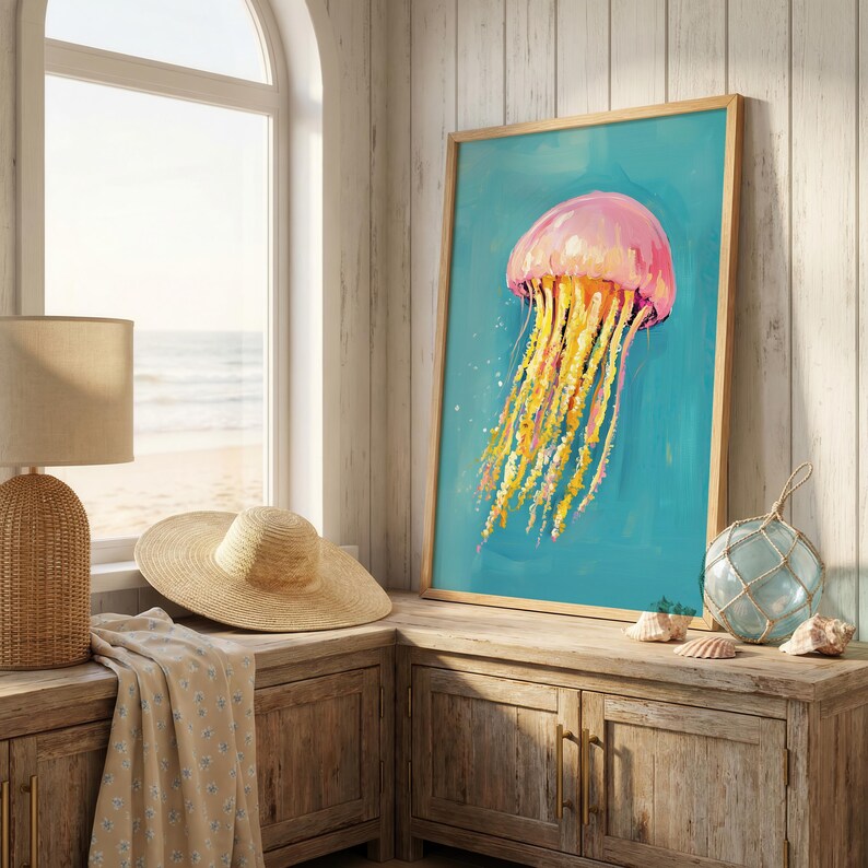 K&ouml;nnte beinhalten: Ein gerahmter Kunstdruck einer Qualle. Die Qualle ist rosa mit gelben und orangefarbenen Tentakeln auf einem t&uuml;rkisfarbenen Hintergrund. Das Kunstwerk wird auf einem Holzschrank mit einer Lampe, einem Hut und dekorativen Gegenst&auml;nden ausgestellt.