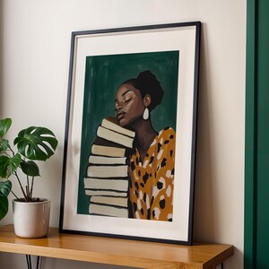 May include: Framed art print featuring a woman with dark skin resting her head on a stack of books. She wears a yellow and brown patterned dress and large white earrings. The background is a dark green color.