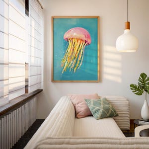 K&ouml;nnte beinhalten: Gerahmter Kunstdruck mit einer rosa-gelben Qualle vor t&uuml;rkisfarbenem Hintergrund. Das Kunstwerk befindet sich in einem Holzrahmen und h&auml;ngt &uuml;ber einem wei&szlig;en Sofa mit dekorativen Kissen. Der Raum hat ein modernes, maritimes Thema.