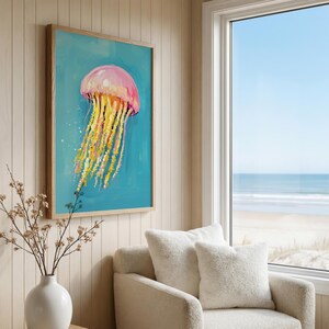 K&ouml;nnte beinhalten: Gerahmtes Gem&auml;lde einer Qualle. Die Qualle ist rosa und gelb mit langen, flie&szlig;enden Tentakeln, vor einem t&uuml;rkisfarbenen Hintergrund. Das Kunstwerk wird an einer hellen Wand in der N&auml;he eines Fensters mit Meerblick ausgestellt.