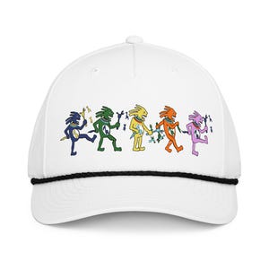 Puede incluir: Gorra de béisbol blanca con borde de cuerda negra. La gorra presenta un gráfico colorido de cinco figuras estilizadas en varios colores, cada una sosteniendo un bastón o instrumento. Las figuras son azules, verdes, amarillas, naranjas y moradas.