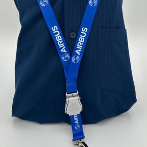 Può includere: Un laccio blu con un fermaglio argentato e un logo "AIRBUS" bianco ripetuto su entrambi i lati.