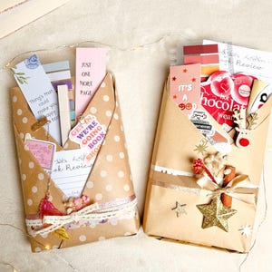 Könnte beinhalten: Zwei braune Pakete, die mit weißen Punkten, goldenen Sternen und einem Band verpackt sind. Ein Paket hat ein rosa-weißes Lesezeichen mit dem Text "Just One More Page". Das andere Paket hat ein rot-weißes Lesezeichen mit dem Text "It's a Good Chocolate Weather".