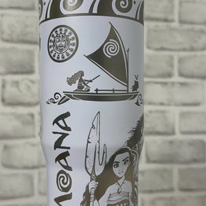 May include: White stainless steel travel mug with a black and white design featuring Moana from the Disney movie Moana. The design includes Moana, Maui, and the ocean.