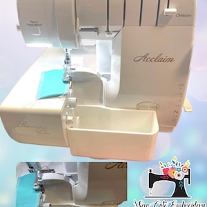 Op de afbeelding: Een witte Baby Lock Acclaim lockmachine met de tekst "Acclaim" en "Revolution Air" zichtbaar. De machine heeft een lichtblauwe stof onder de naald en een afvalbak. De afbeelding bevat ook de tekst "Push to Thread Needles".