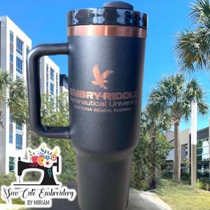 May include: Black and copper travel mug with a black handle. The mug has the text "Embry-Riddle Aeronautical University Daytona Beach, Florida" and a black bird logo.