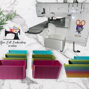 May include: A white sewing machine with a colorful logo that says "Sew Cute Embroidery by Miriam". There are several colorful plastic storage bins in the image.