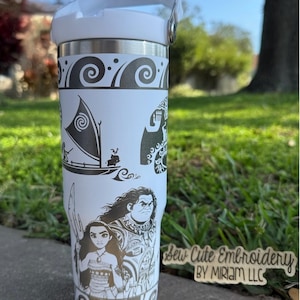 May include: White stainless steel tumbler with a black and white design featuring characters from the animated film Moana. The design includes Moana, Maui, and a sailing canoe. The tumbler has a black lid with a carrying handle. The text "Sew Cute Embroidery by Miriam LLC" is visible in the lower right corner of the image.