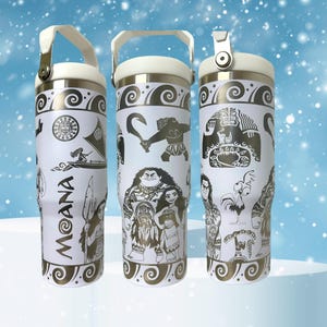May include: Three white stainless steel tumblers with a Moana theme. The tumblers feature black and gold designs of Moana, Maui, and other characters from the film. The tumblers have a white lid with a black handle.