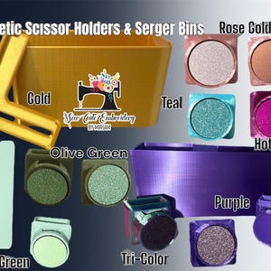 May include: An assortment of magnetic scissor holders and serger bins in a variety of colours, including gold, olive green, sage green, teal, hot pink, rose gold, purple, and tri-colour. The bins are made of plastic and have a textured surface. The holders are made of metal and have a magnetic base. The text "Saw Cute Embroidery by Miriam" is visible on the gold bin.