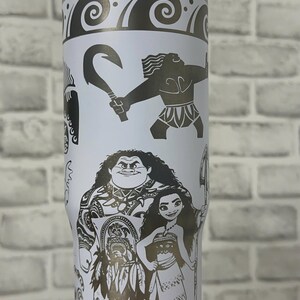 May include: White stainless steel travel tumbler with a black and white design featuring characters from the animated movie Moana. The design includes Maui, Moana, and a hook.