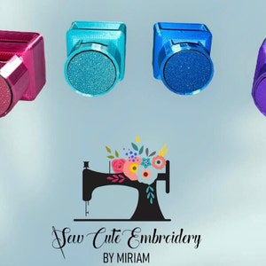 May include: Four square-shaped plastic needle minders in magenta, teal, blue, and purple, each featuring a circular magnetic front. Below them is a black silhouette logo of a sewing machine with a floral arrangement and the text Sew Cute Embroidery BY MIRIAM.