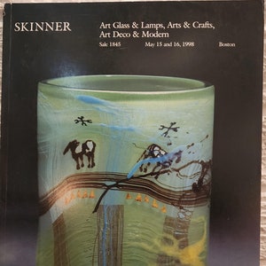 May include: A green glass vase with a textured surface and abstract designs in brown, blue, and yellow. The vase has a wide mouth and a rounded bottom.