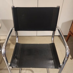 May include: A black leather and chrome chair with a footrest. The chair has a simple design with a curved back and a wide seat.