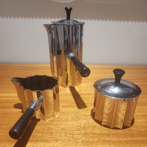 Könnte beinhalten: Ein Satz aus drei versilberten Kaffee- und Zucker-Servierstücken mit schwarzen Griffen. Die Stücke haben ein geriffeltes Design und sind in ausgezeichnetem Zustand.