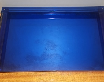 Peut inclure: Un plateau en verre bleu avec un bord surélevé. Le plateau est vide et a un léger éclat.