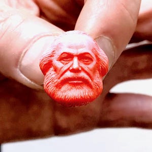 Puede incluir: Una pequeña escultura roja detallada de la cara de un hombre con barba.