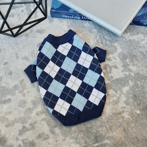 Puede incluir: Un suéter para perro azul y blanco con estampado de rombos y mangas cortas.