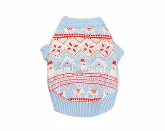 May include: A light blue knitted sweater with a red and white snowflake pattern. The sweater has a festive holiday design with small houses and reindeer.