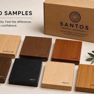 Op de afbeelding: Vierkante houtmonsters in diverse kleuren, waaronder Naturel Eik, Walnoot, Ebben, Esdoorn en Gouden Eik. Elk monster is gelabeld met de houtsoort. Een kartonnen doos met het logo "SANTOS - WOOD COMPANY" is zichtbaar.