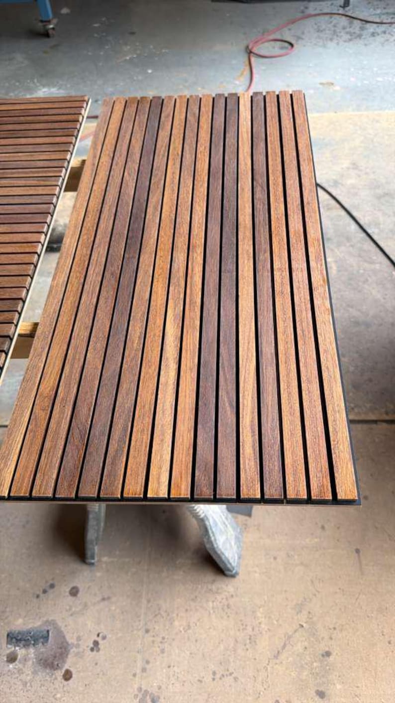 May include: A rectangular acoustic wall panel featuring vertical wooden slats in a medium brown tone with visible wood grain, separated by narrow black felt gaps. The panel has a clean, linear design with uniform spacing between each wooden strip.