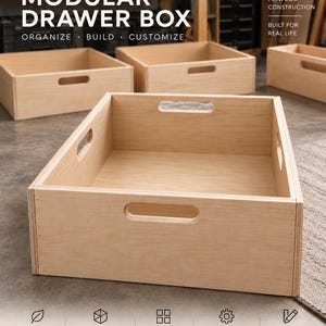 May include: A light-colored wooden modular drawer box with cut-out handles on each side. The text MODULAR DRAWER BOX ORGANIZE BUILD CUSTOMIZE is visible at the top, with additional text PREMIUM PLYWOOD CONSTRUCTION BUILT FOR REAL LIFE.