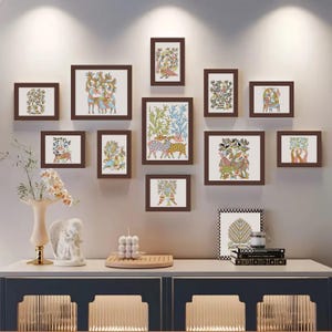 May include: A gallery wall of framed art prints with brown frames, showcasing vibrant illustrations of animals and plants. The artwork is mounted on a light grey wall above a white cabinet with a blue base. Decorative items are on the cabinet.